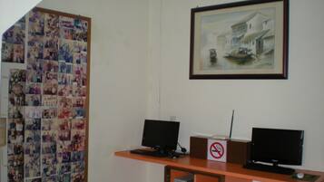A room with two computer monitors on a desk, a framed painting above, and a collage of photos on the wall.