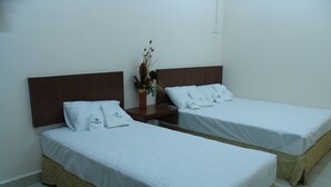 Two single beds with white linens, a wooden headboard, a nightstand with a vase of flowers, and a tiled floor. - Friendship Motel (George Town)