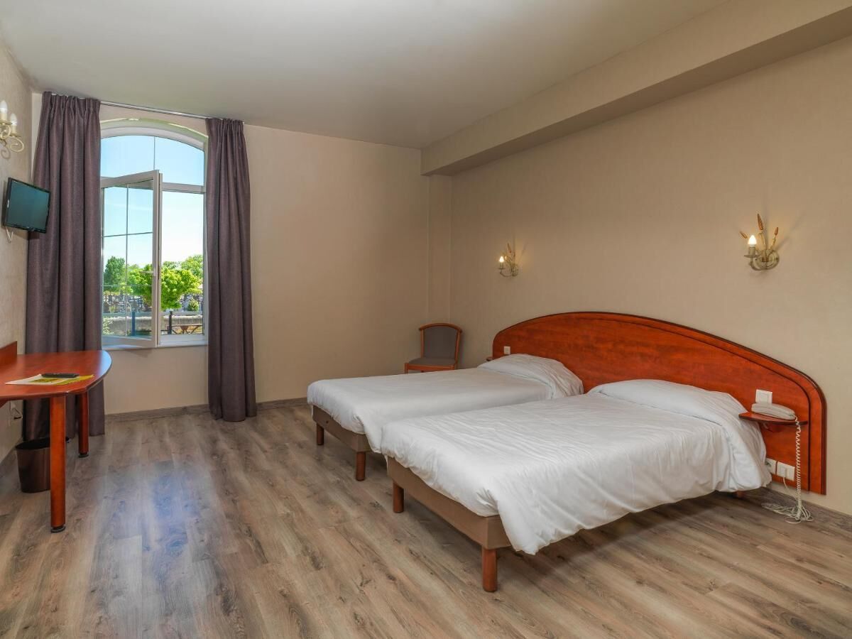 Une chambre d’hôtel avec deux lits, un bureau, une chaise, une télévision et une fenêtre avec des rideaux.