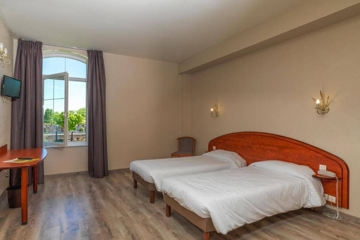 A hotel room with two beds, a desk, a chair, a TV, and a window with curtains.
