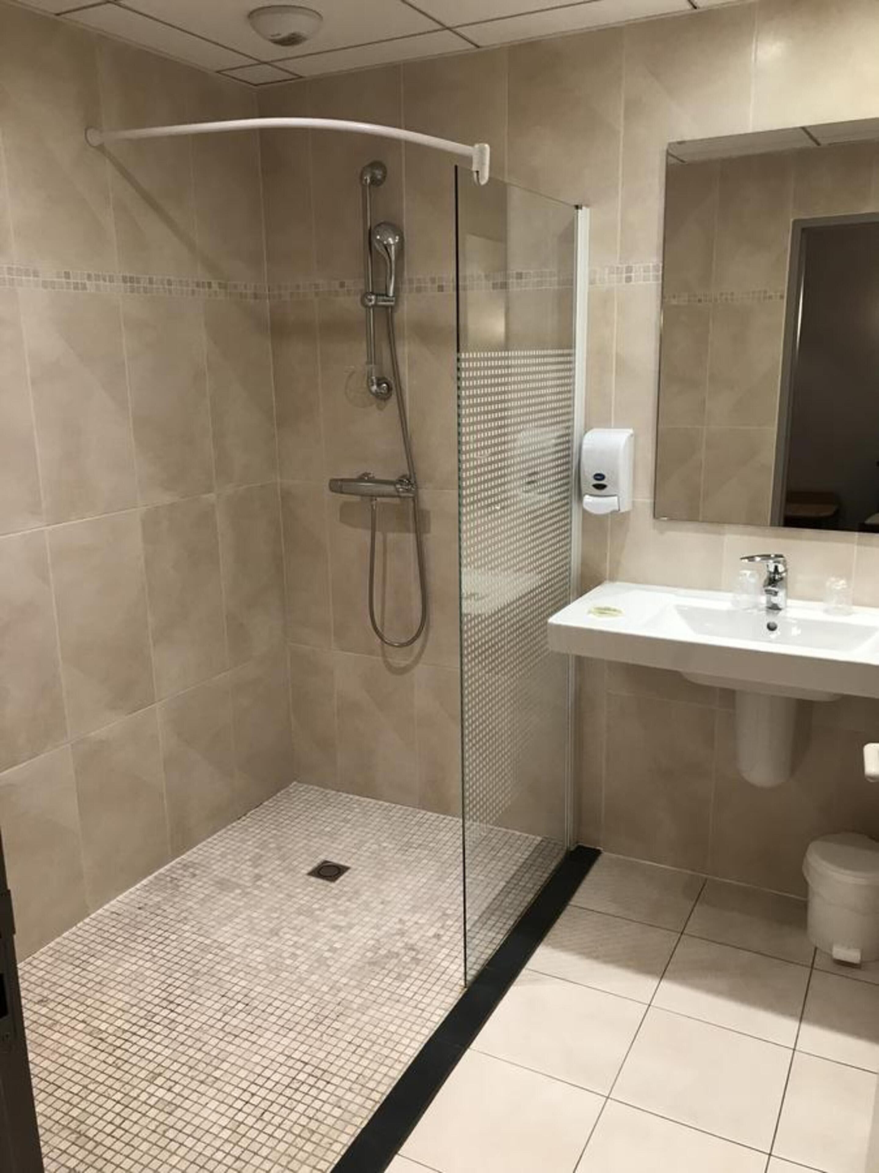 Un baño moderno con ducha de vidrio, lavamanos blanco y espejo sobre el lavamanos.