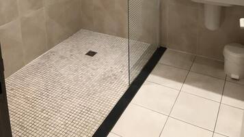 Un baño moderno con ducha de vidrio, lavamanos blanco y espejo sobre el lavamanos.