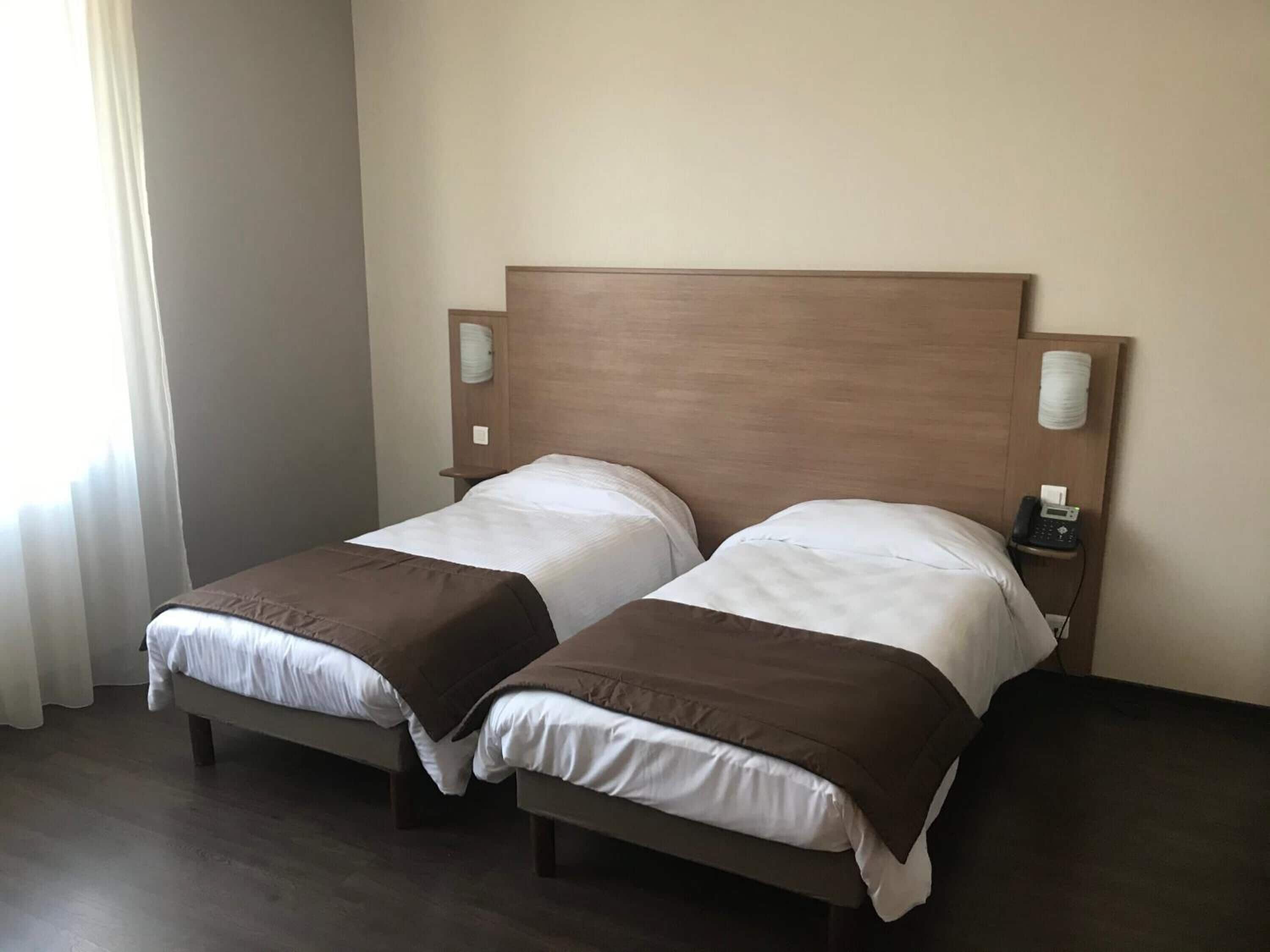 A double bed with a wooden headboard, two bedside tables with lamps, and a window with curtains.