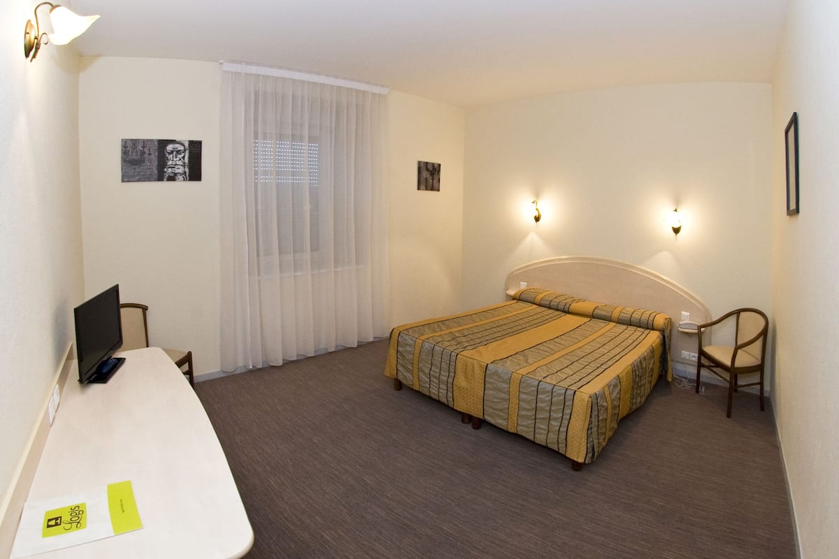 Ein Hotelzimmer mit einem Bett, einem Schreibtisch mit Computer, einem Stuhl und zwei Wandleuchten.