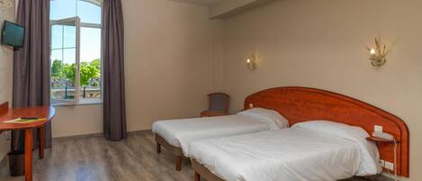 A hotel room with two beds, a desk, a chair, a TV, and a window with curtains.