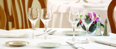 A dining table set with plates, cutlery, and wine glasses, with a vase of flowers and salt and pepper shakers on the table.