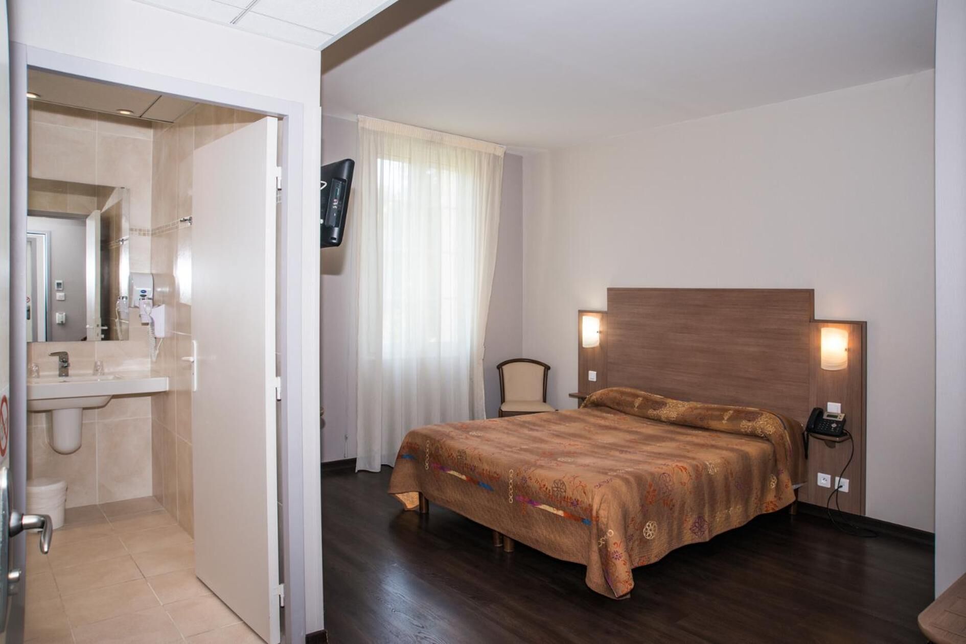 Une chambre d’hôtel comprenant un lit, des lampes de chevet, une télévision et une salle de bain avec un lavabo et un miroir.