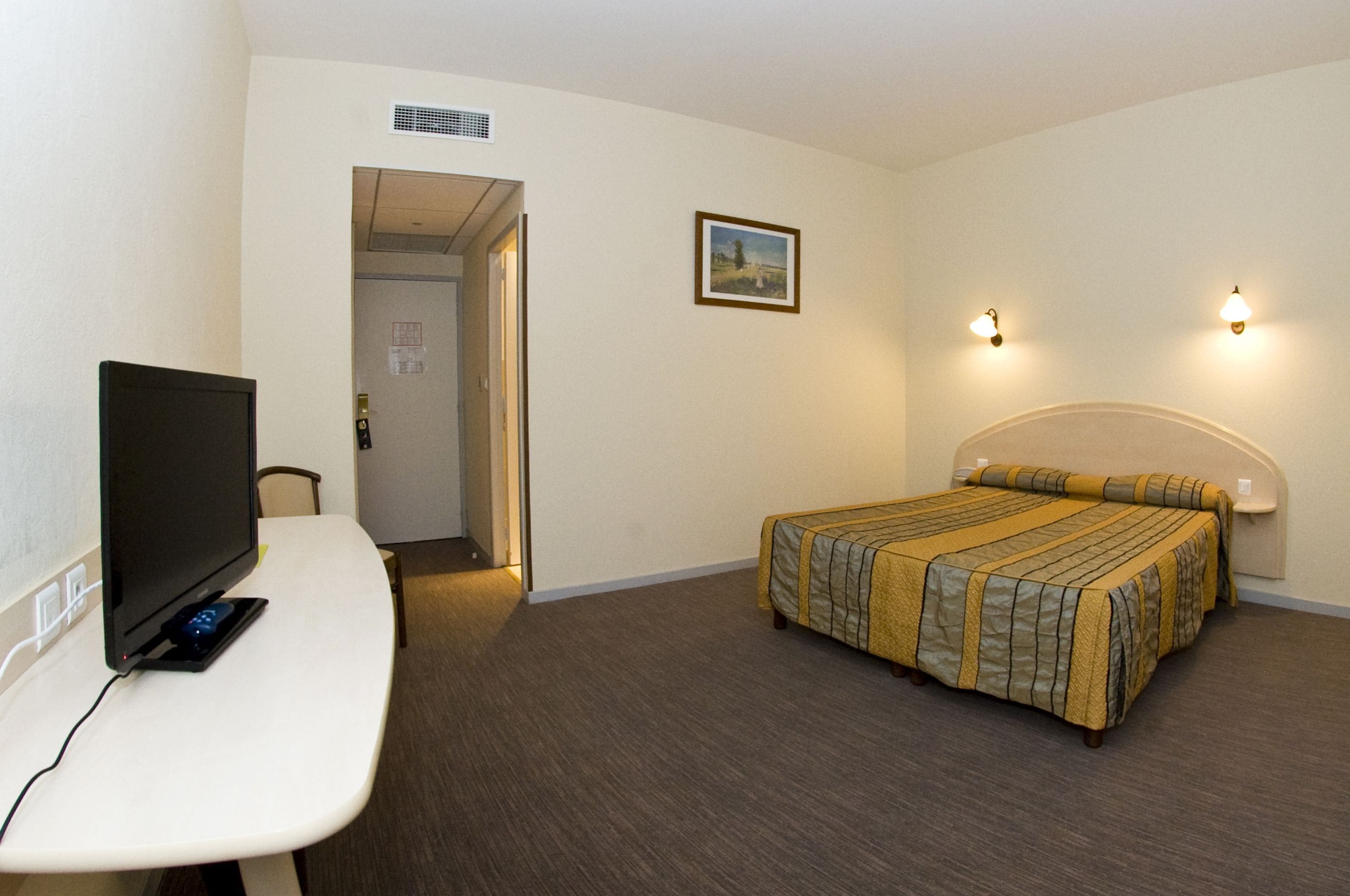 A hotel room with a bed, a desk with a computer, and a television.