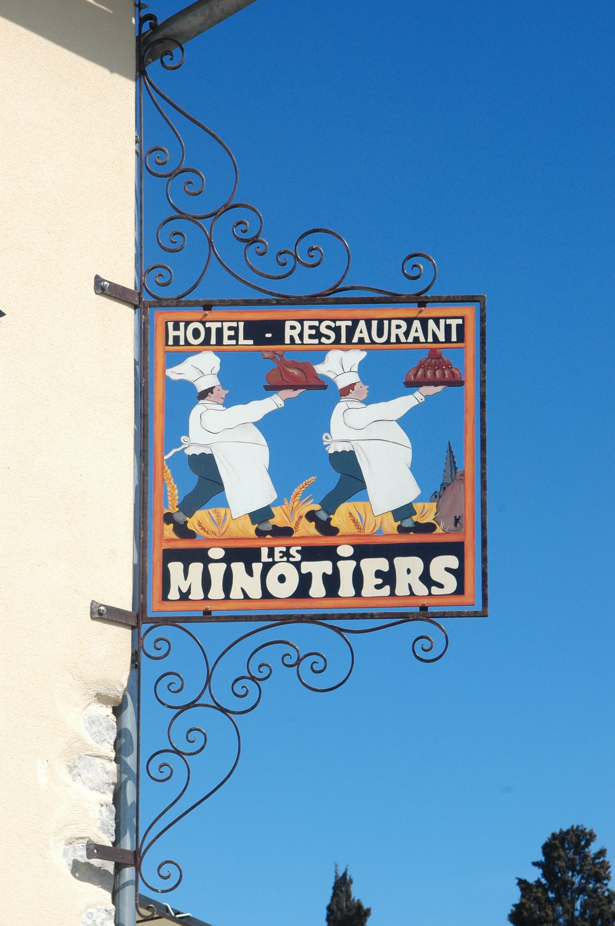 A vintage sign for a hotel and restaurant named "Les Minotiers," featuring two chefs holding dishes.