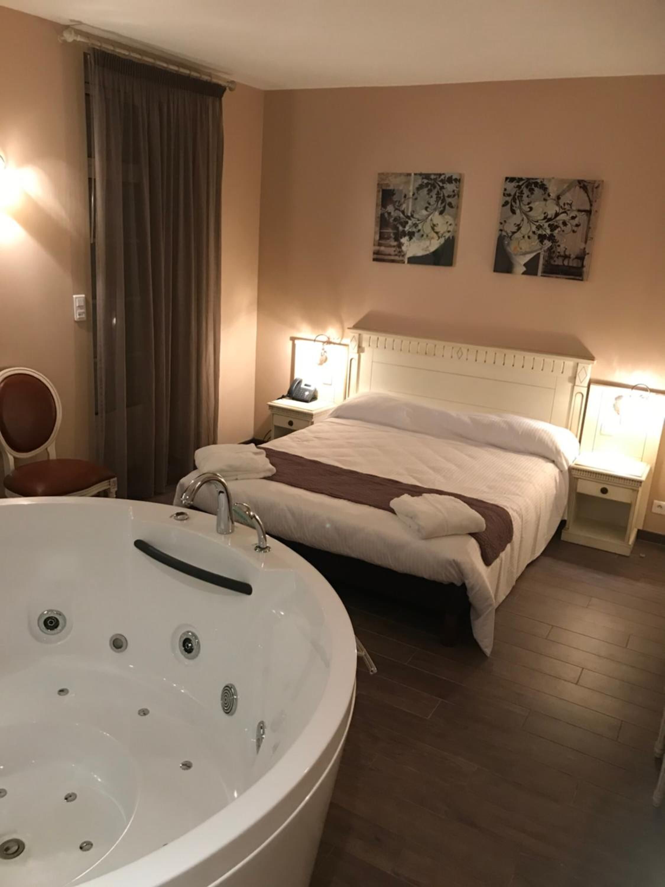 Ein Hotelzimmer mit einer großen, weißen Badewanne, einem Bett mit weißer Bettwäsche, zwei Nachttischlampen und einem Sessel.
