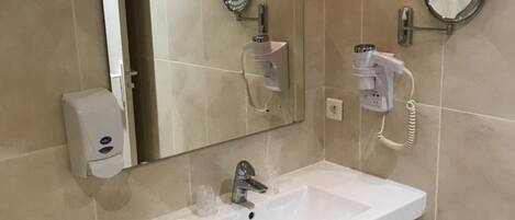 A bathroom with a large mirror, a sink, a handheld showerhead, a towel dispenser, and a toilet.