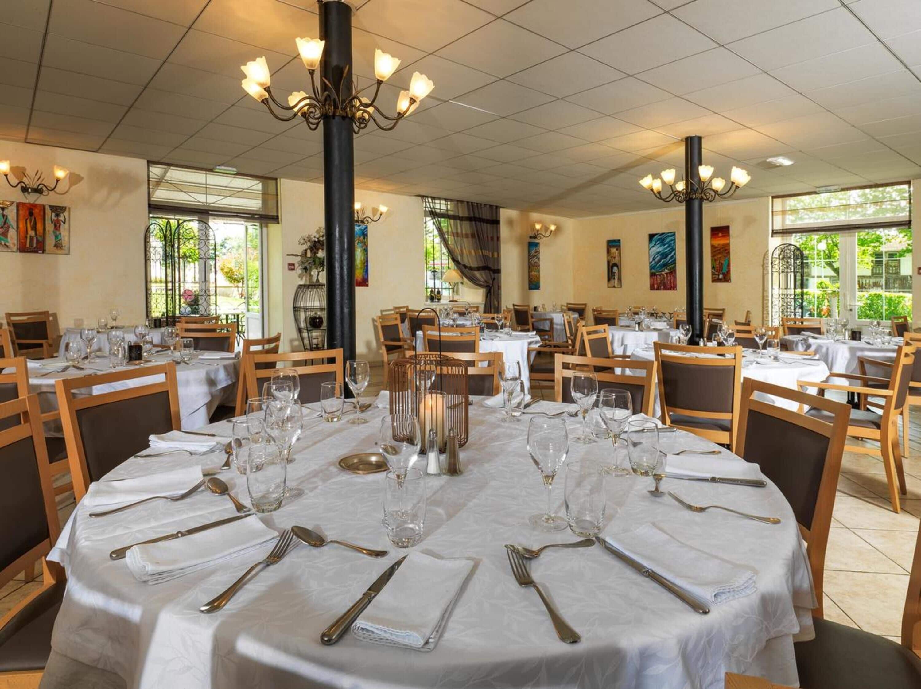 A dining area with round tables set for service, featuring white tablecloths, silverware, and wine glasses.