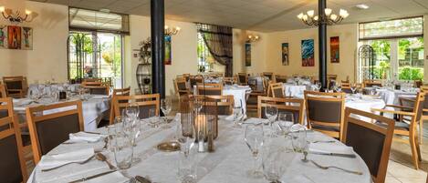 A dining area with round tables set for service, featuring white tablecloths, silverware, and wine glasses.