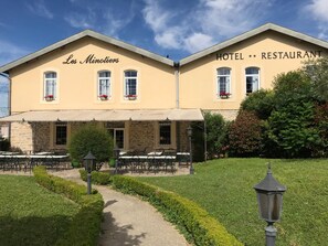 Les Minotiers Hotel offers a charming outdoor seating area surrounded by a beautifully maintained garden and hedges.
