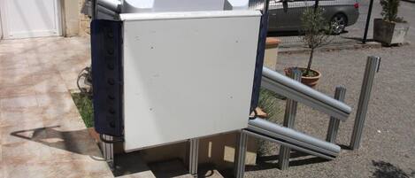 A large, white, metallic object with a handle, possibly a piece of equipment, placed on a tiled surface outdoors.