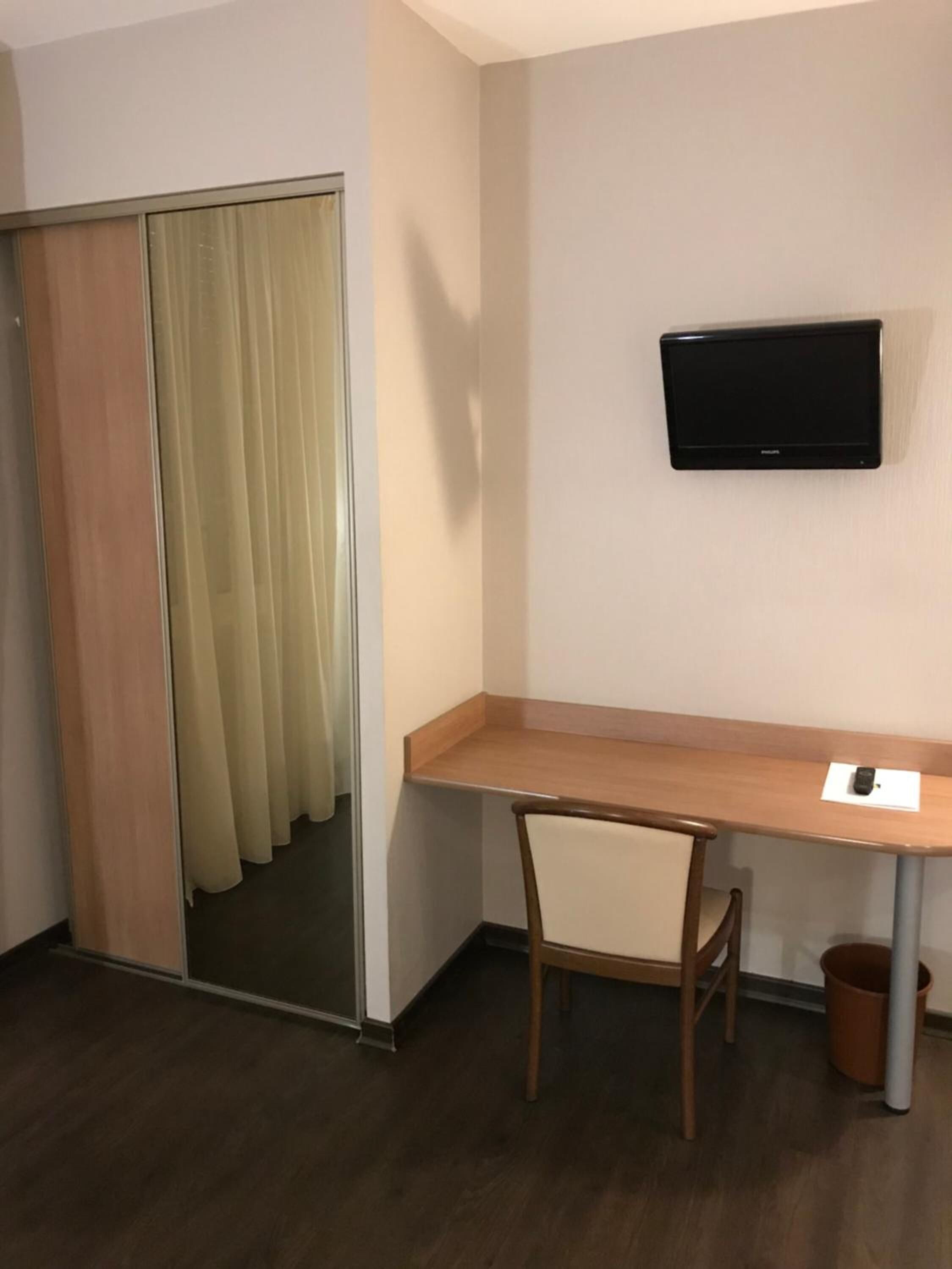 Habitación de hotel con un escritorio de madera, una silla, televisor montado en la pared y una puerta corredera con cortinas.