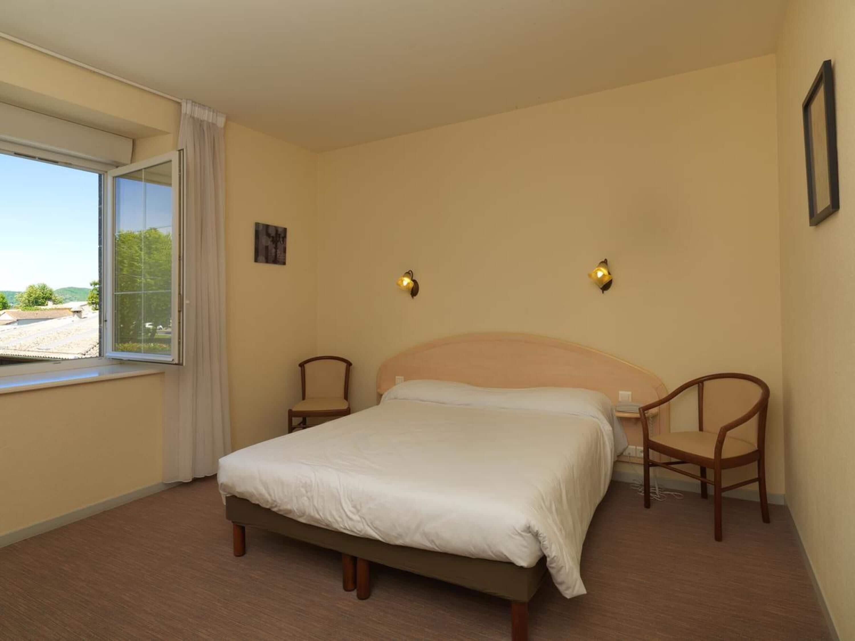 A bedroom with a bed, two chairs, a window, and two wall-mounted lights.