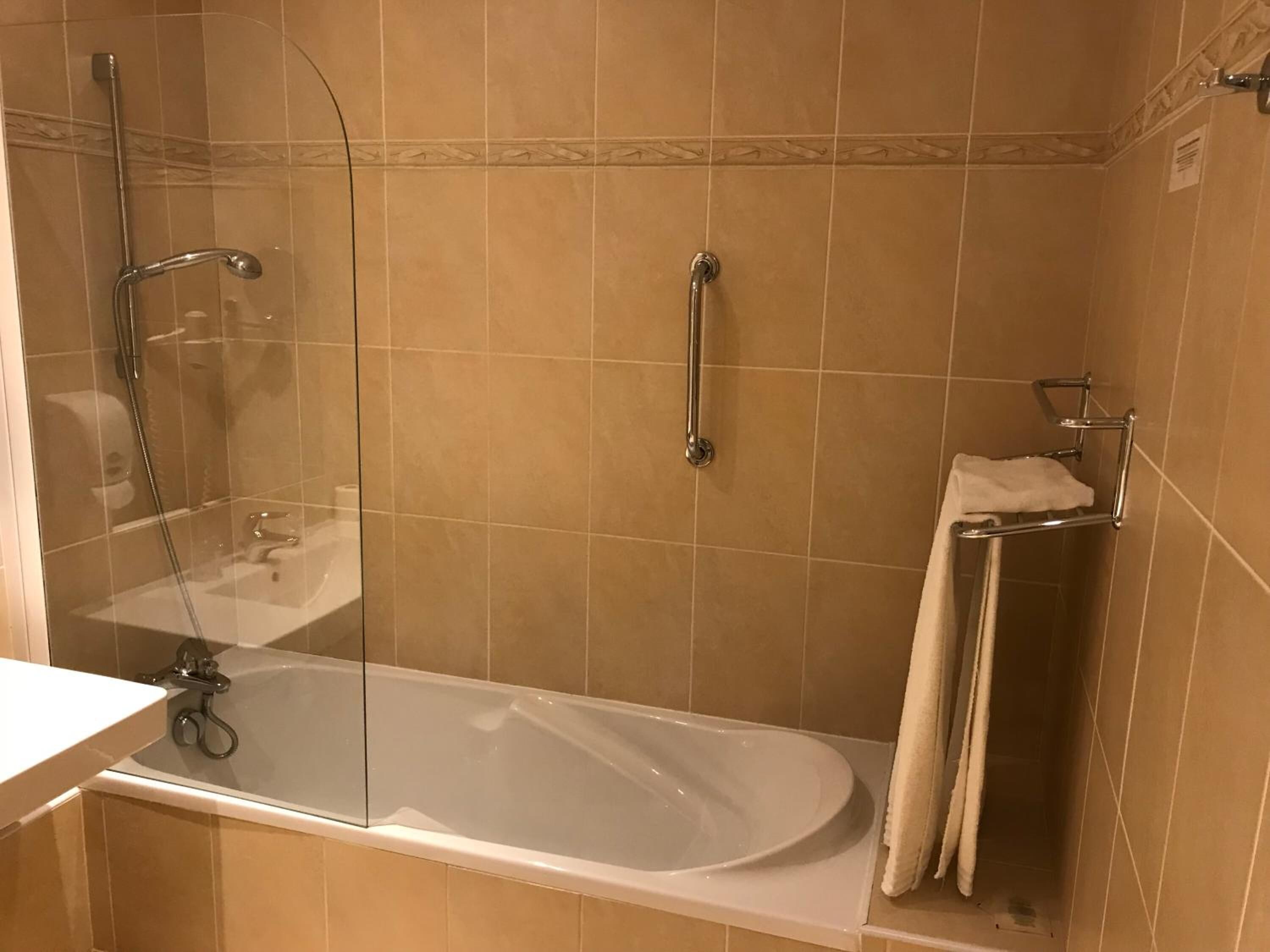 A bathroom with a glass-enclosed shower, a white bathtub, and a towel rack.