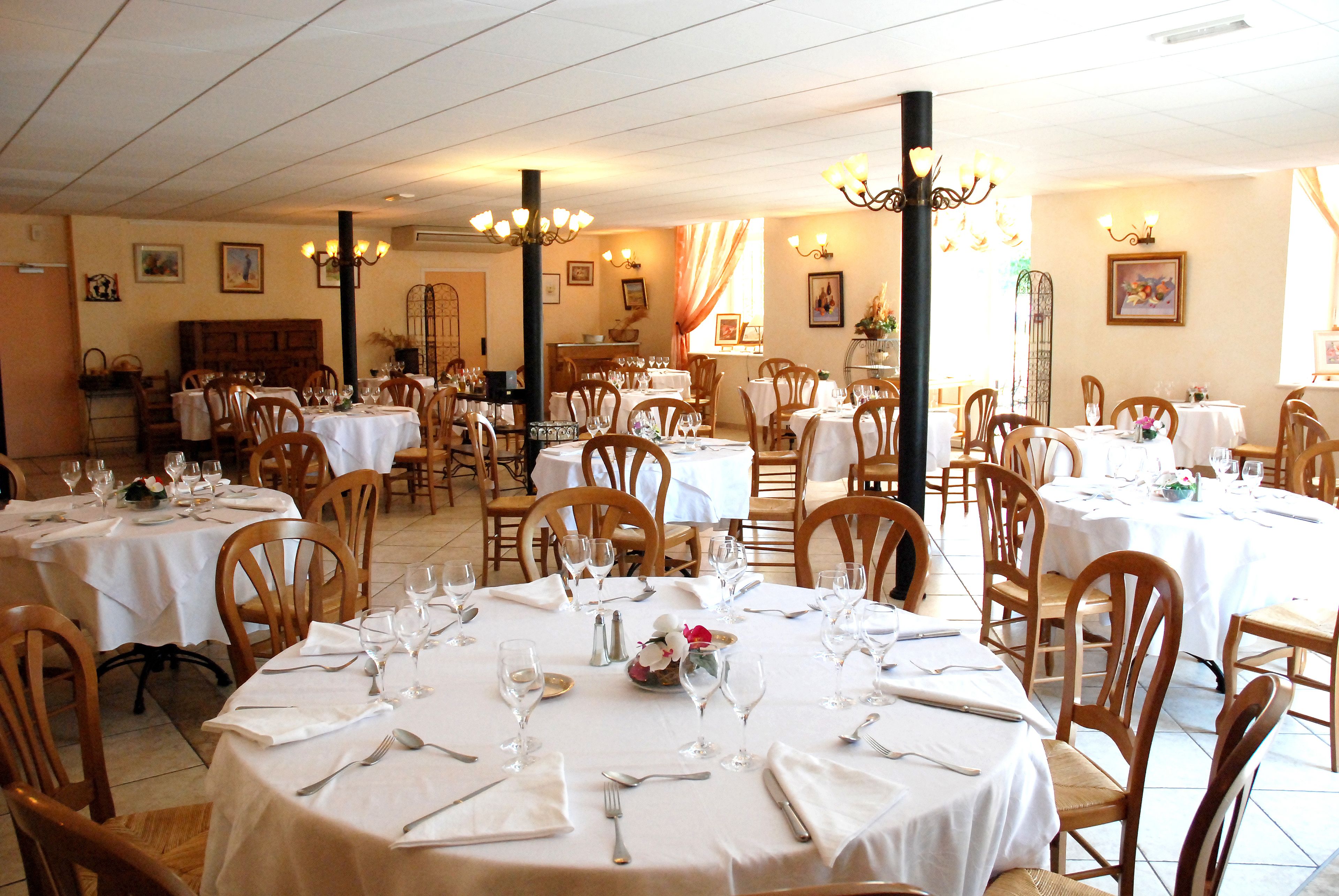 Een restaurant met meerdere ronde tafels, gedekt met witte tafellakens, stoelen en bestek.