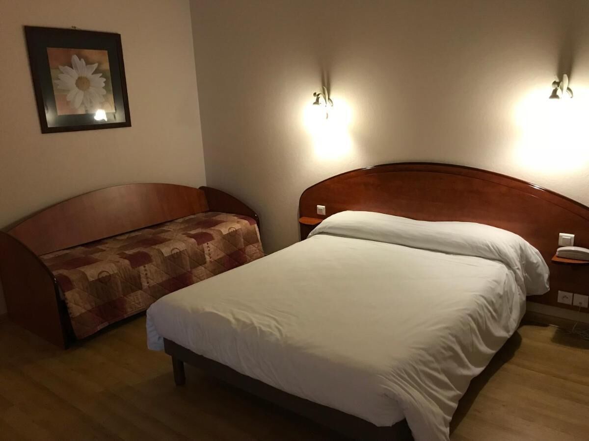 Une chambre d’hôtel avec un lit, un canapé et deux lampes fixées au mur.