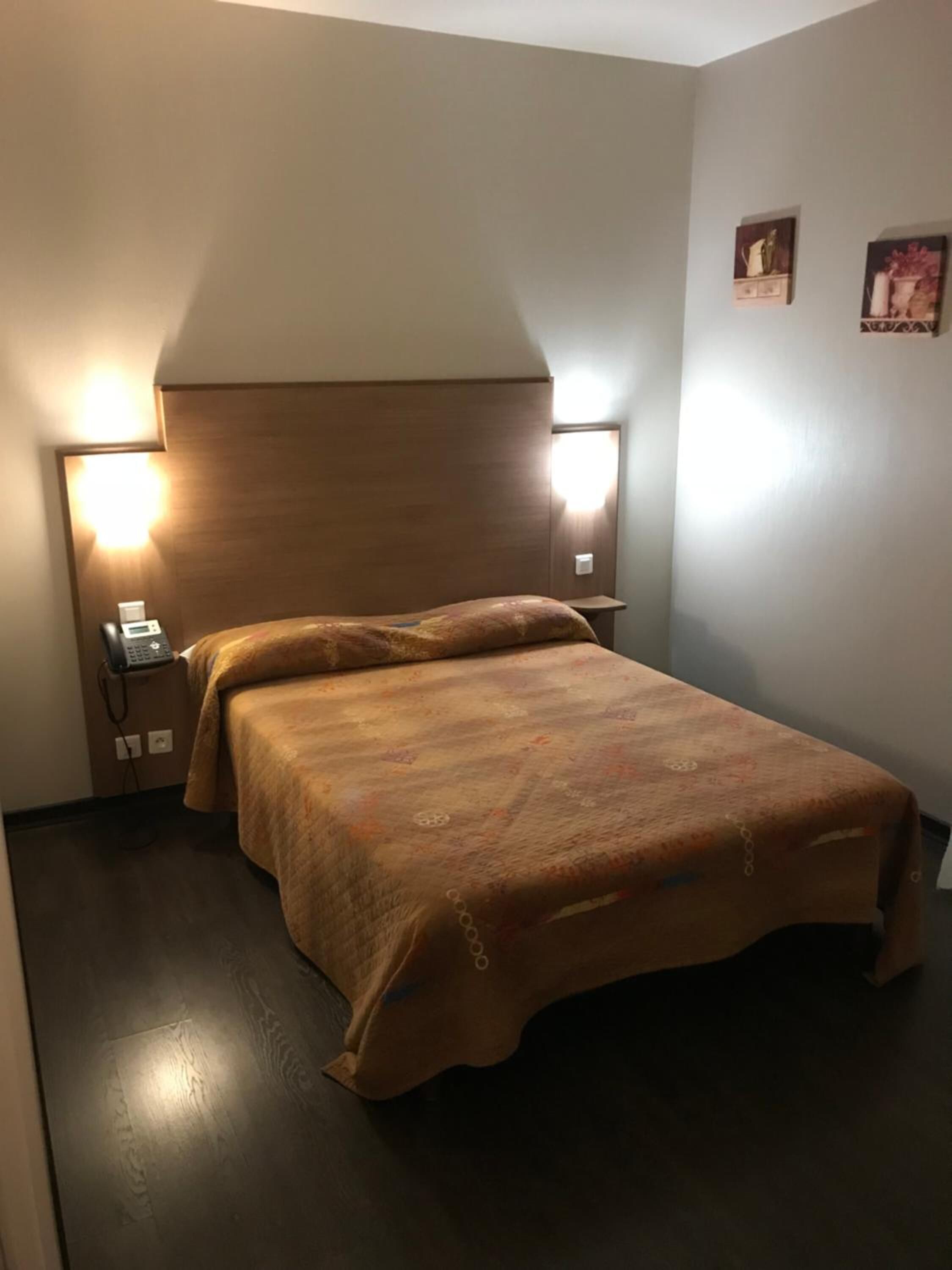 Et hotelværelse med sengebordlamper, en seng med et mønstret sengetæppe og en telefon på skuffen.