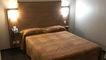 Et hotelværelse med sengebordlamper, en seng med et mønstret sengetæppe og en telefon på skuffen.
