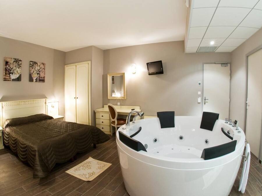 Een slaapkamer met een groot bad, een bed, een bureau en een stoel.