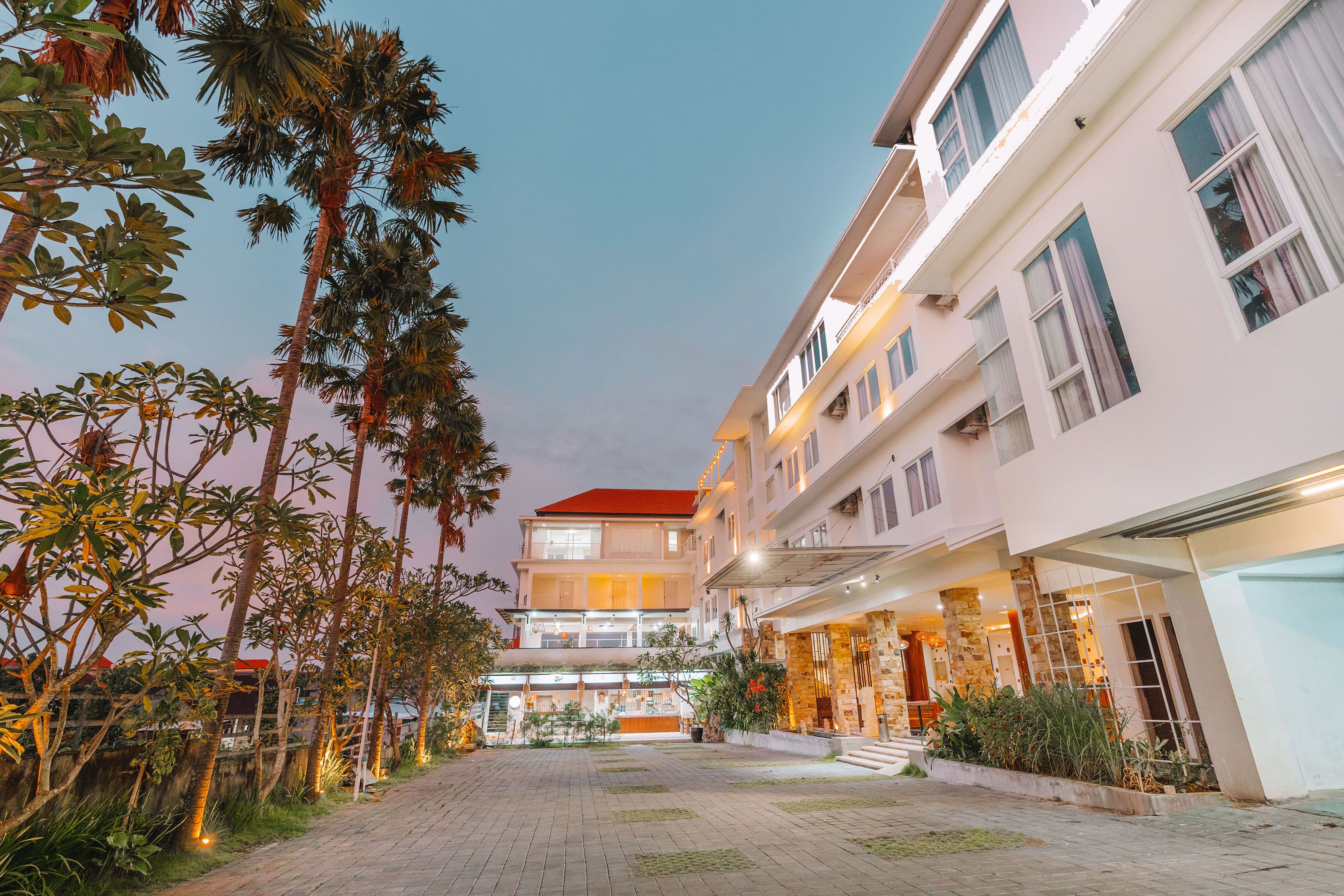 A multi-story hotel with a red roof, a covered outdoor area with plants, and a paved courtyard.