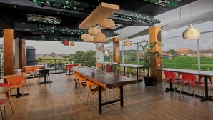 A spacious dining area with wooden tables and chairs, large windows offering a view of the countryside, and hanging wicker lamps. - The Salak Hotel (Denpasar)