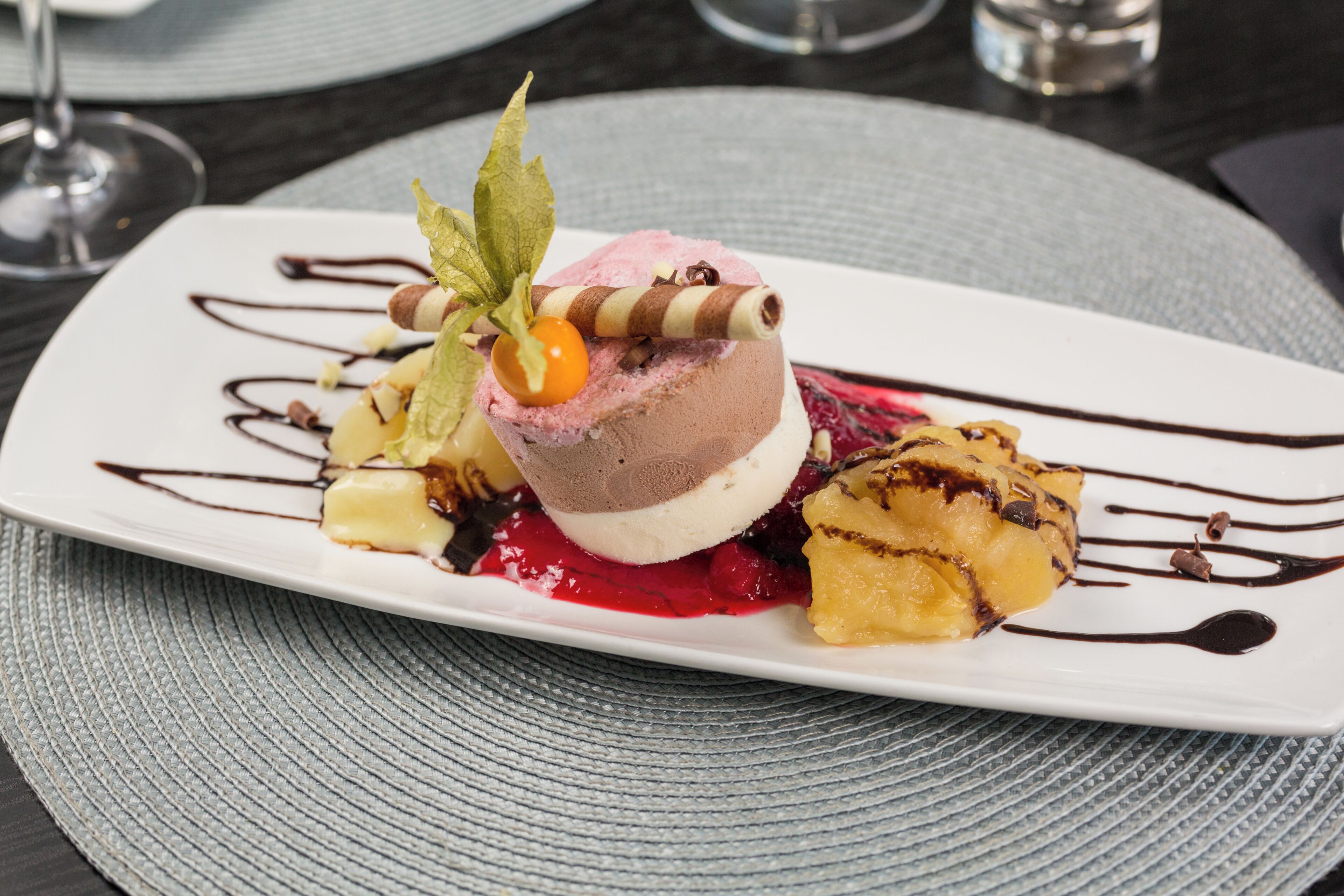 Ein Dessertteller mit einer Kugel Eis, Beerenkompott und Schokoladenglasur.