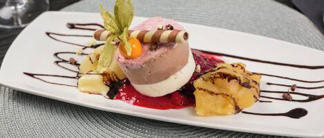 Ein Dessertteller mit einer Kugel Eis, Beerenkompott und Schokoladenglasur.