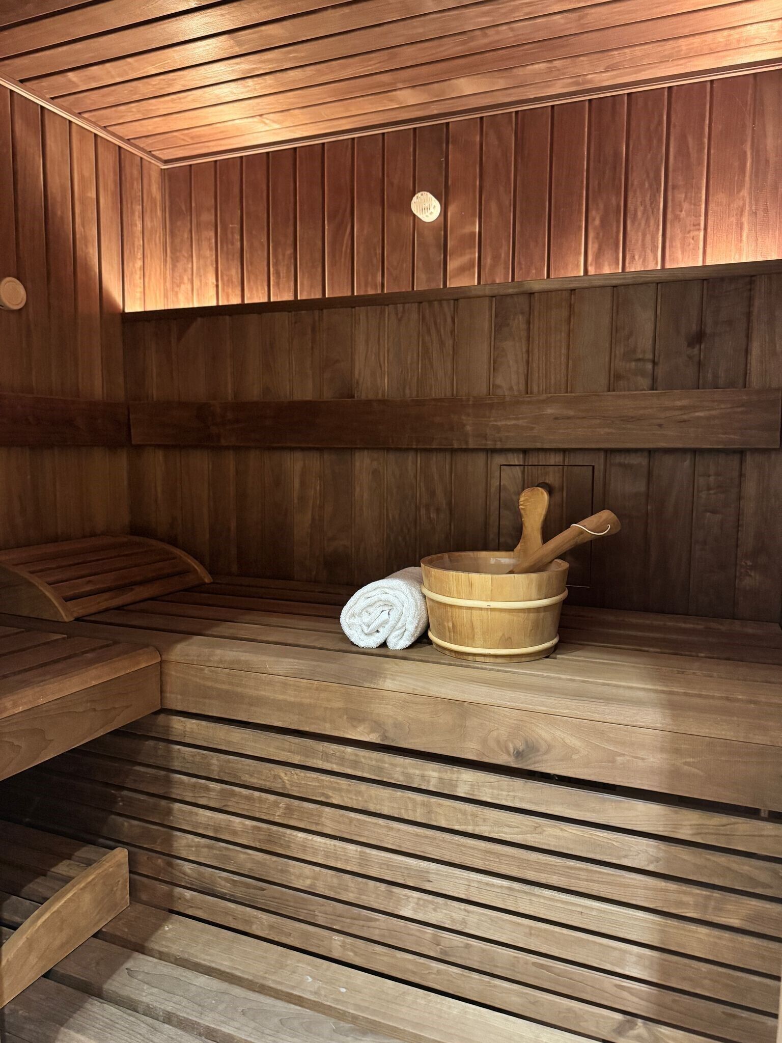 A wooden sauna with benches, a wooden bucket, and a rolled towel.