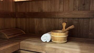 A wooden sauna with benches, a wooden bucket, and a rolled towel.