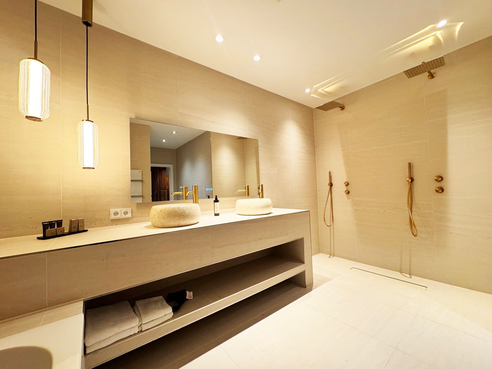 Une salle de bain moderne dotée d’un grand miroir, de deux vasques, d’une douche et d’étagères intégrées.