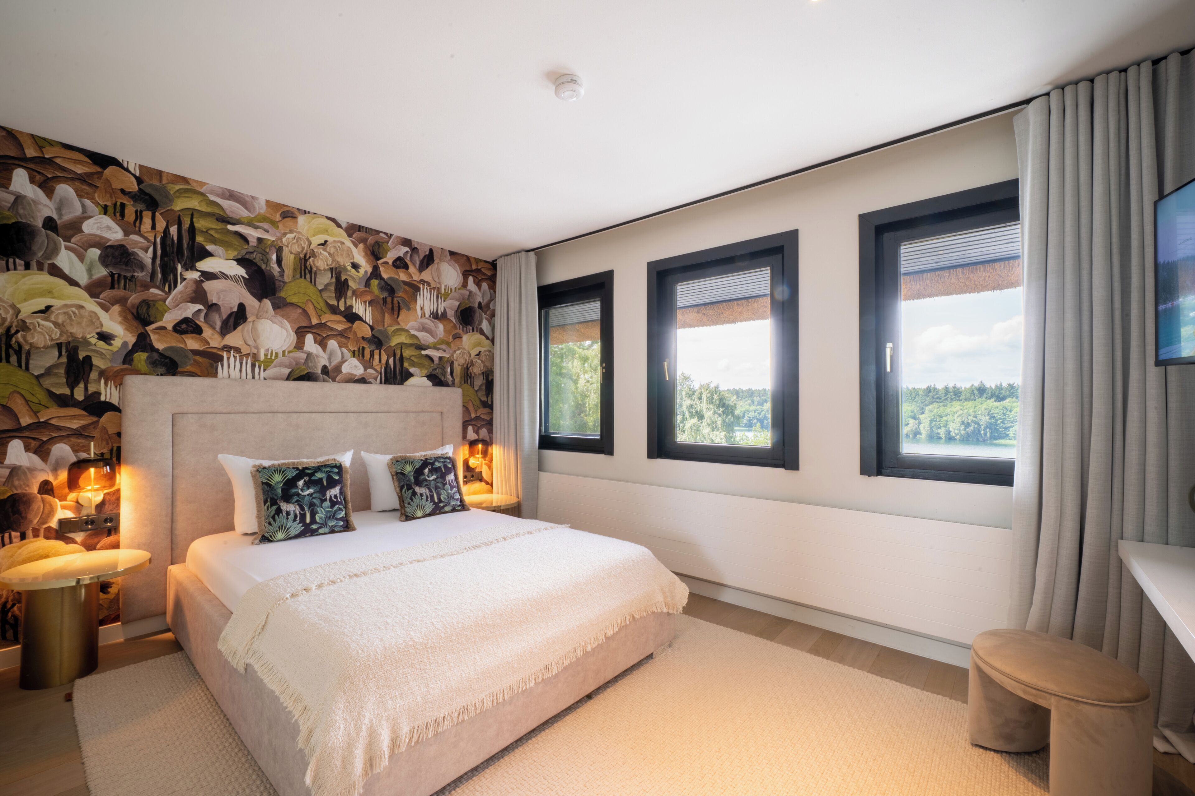 Un dormitorio con una cama grande, un mural en la pared y tres ventanas.