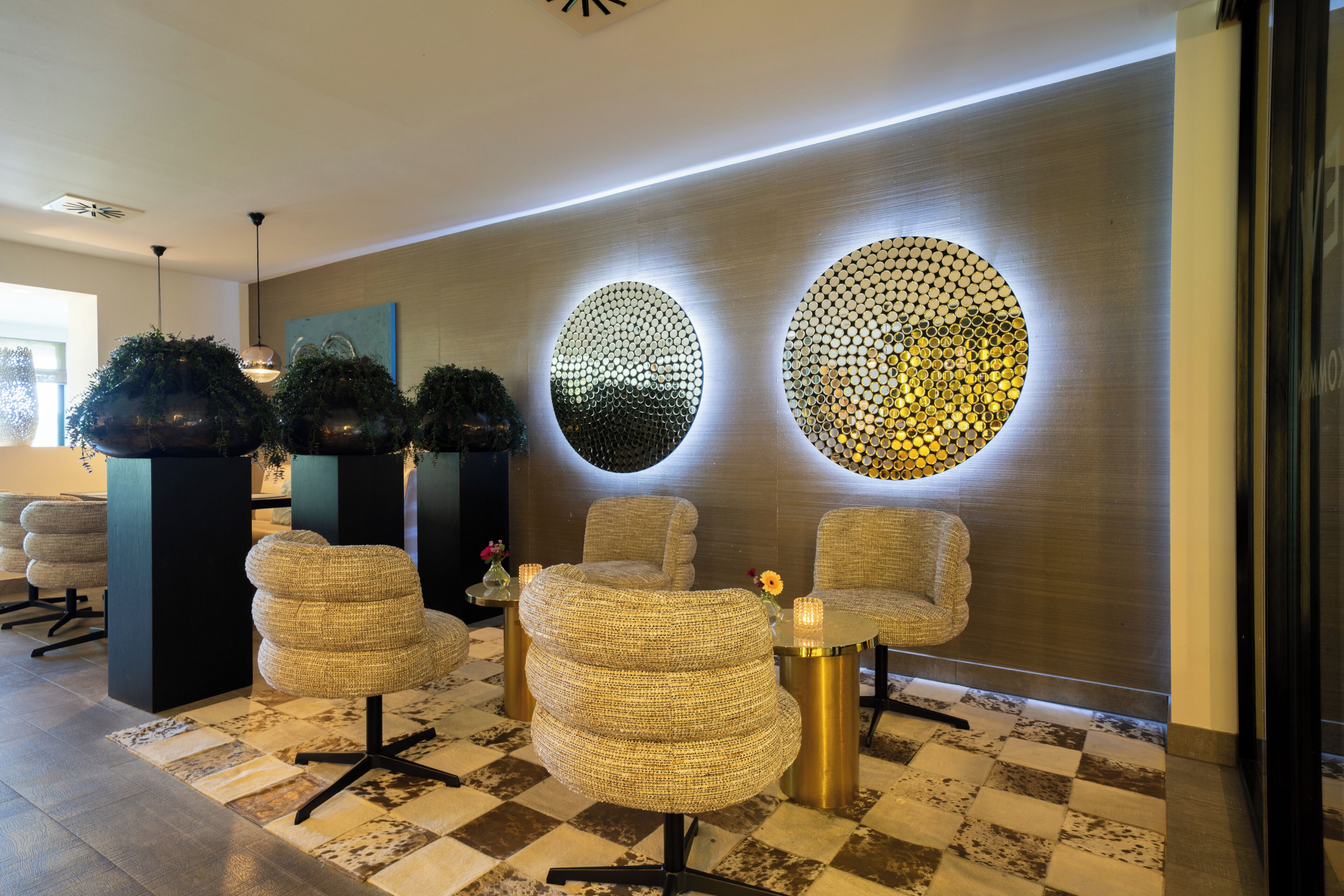 A lobby with a checkered floor, round woven chairs, a wall with circular light fixtures, and a modern reception desk.