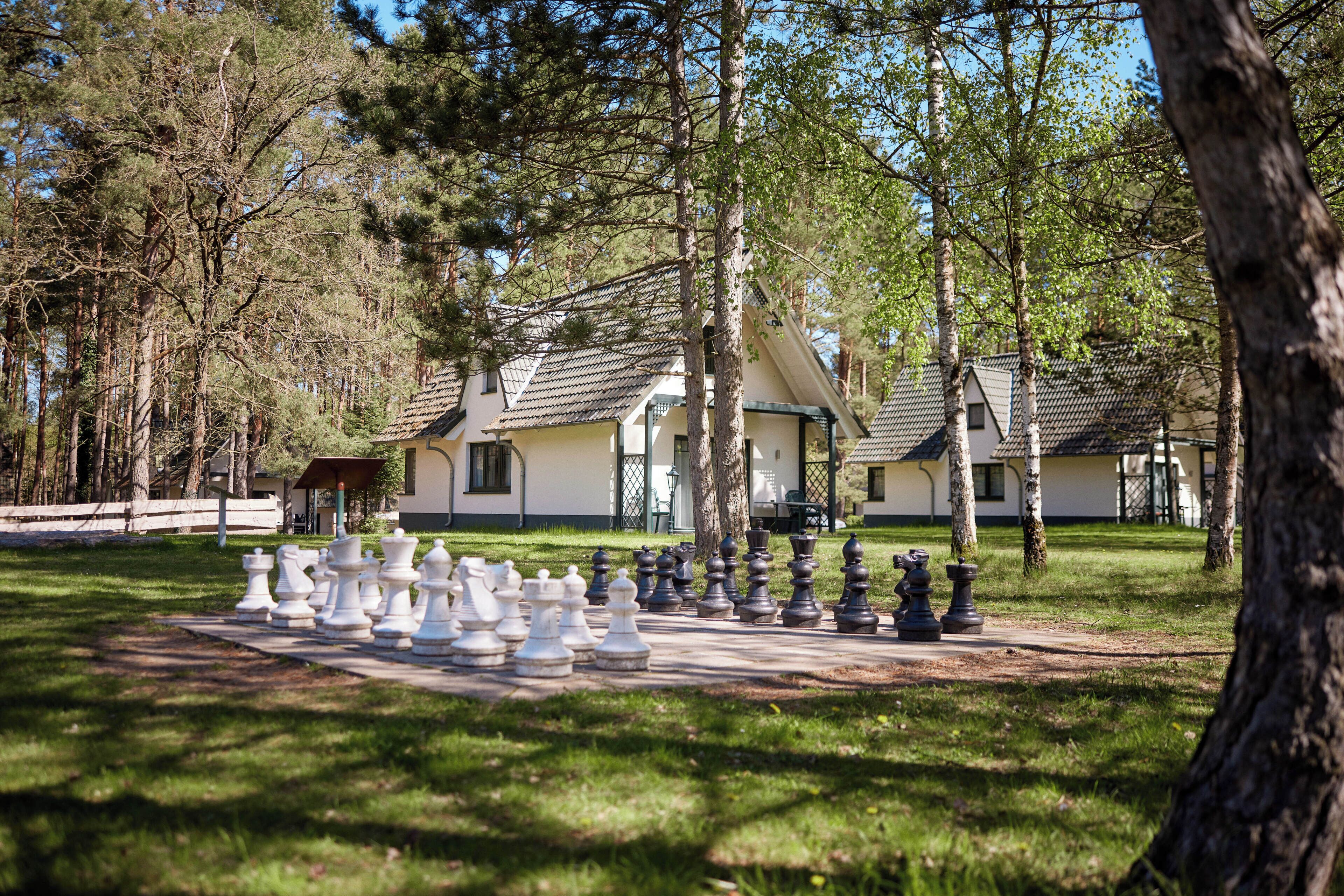 A chessboard set up outdoors with trees and a building in the background.