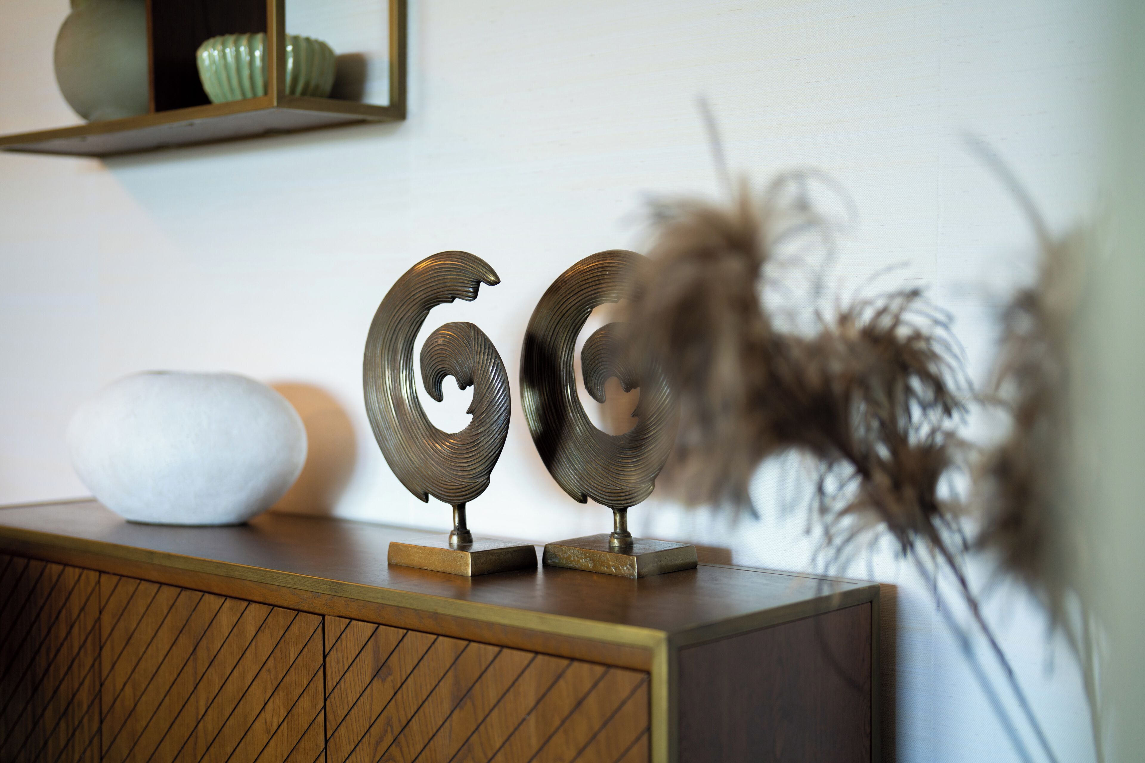 A wooden cabinet with decorative metal numbers, a white vase, and a mirror reflecting a green bowl.