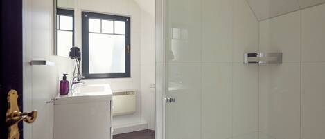 A bathroom with a white sink, a mirror, a window, and a shower area.