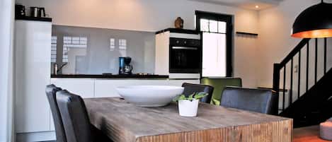 A modern kitchen with white cabinets, a black oven, and a wooden dining table with a white bowl and a potted plant.