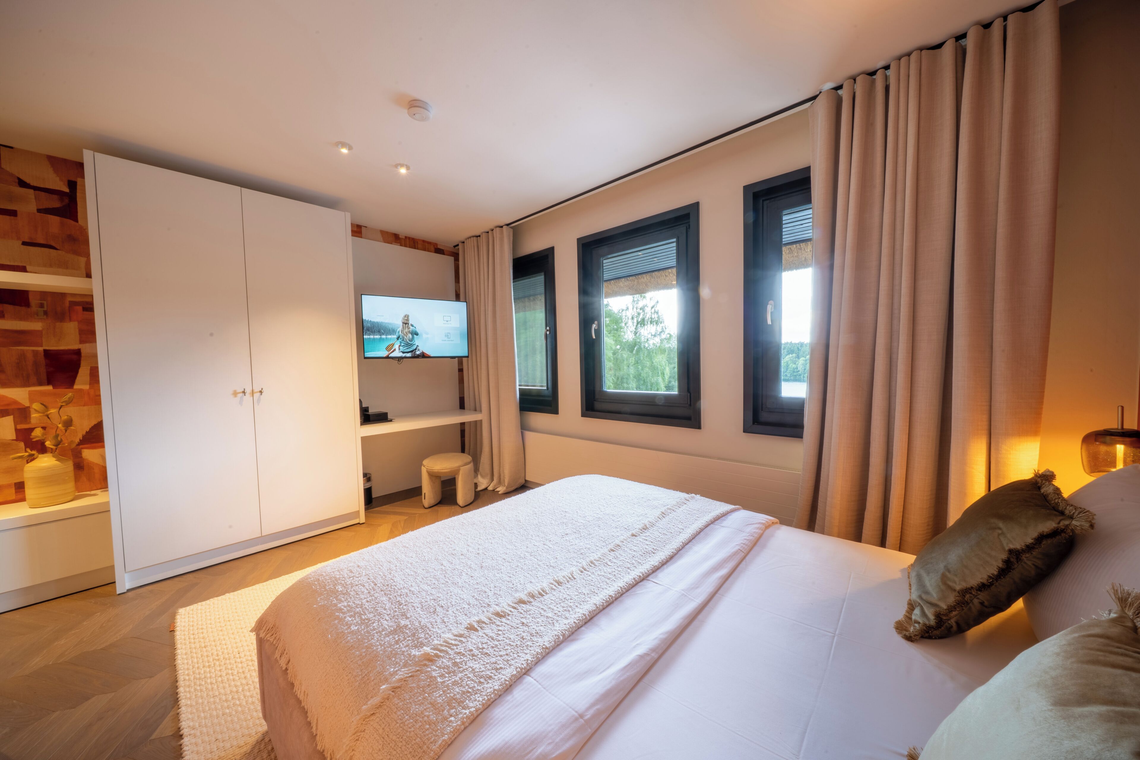 Een moderne slaapkamer met een groot bed, een televisie, een garderobe en een raam met gordijnen.