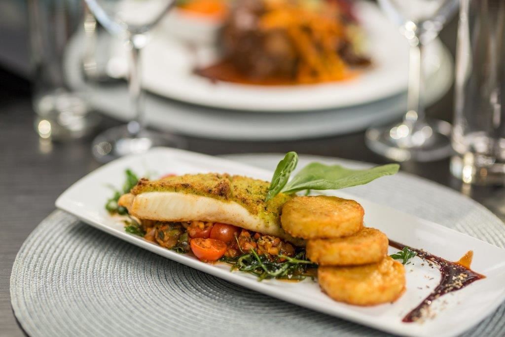 A plated dish with fish, vegetables, and a garnish on a white plate.