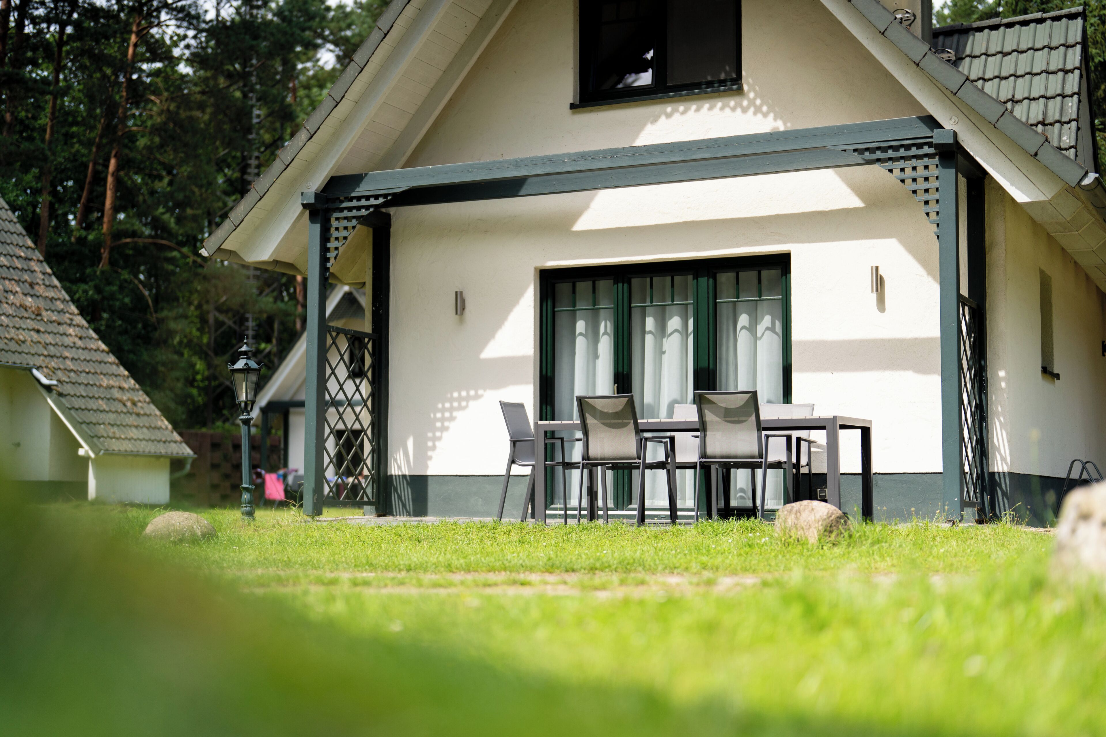 Een huis met een overdekte patio, een eethoek met stoelen en een tafel, en een raam met uitzicht op de omgeving.