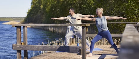 Zwei Personen üben Yoga auf einem Holzsteg an einem Gewässer.