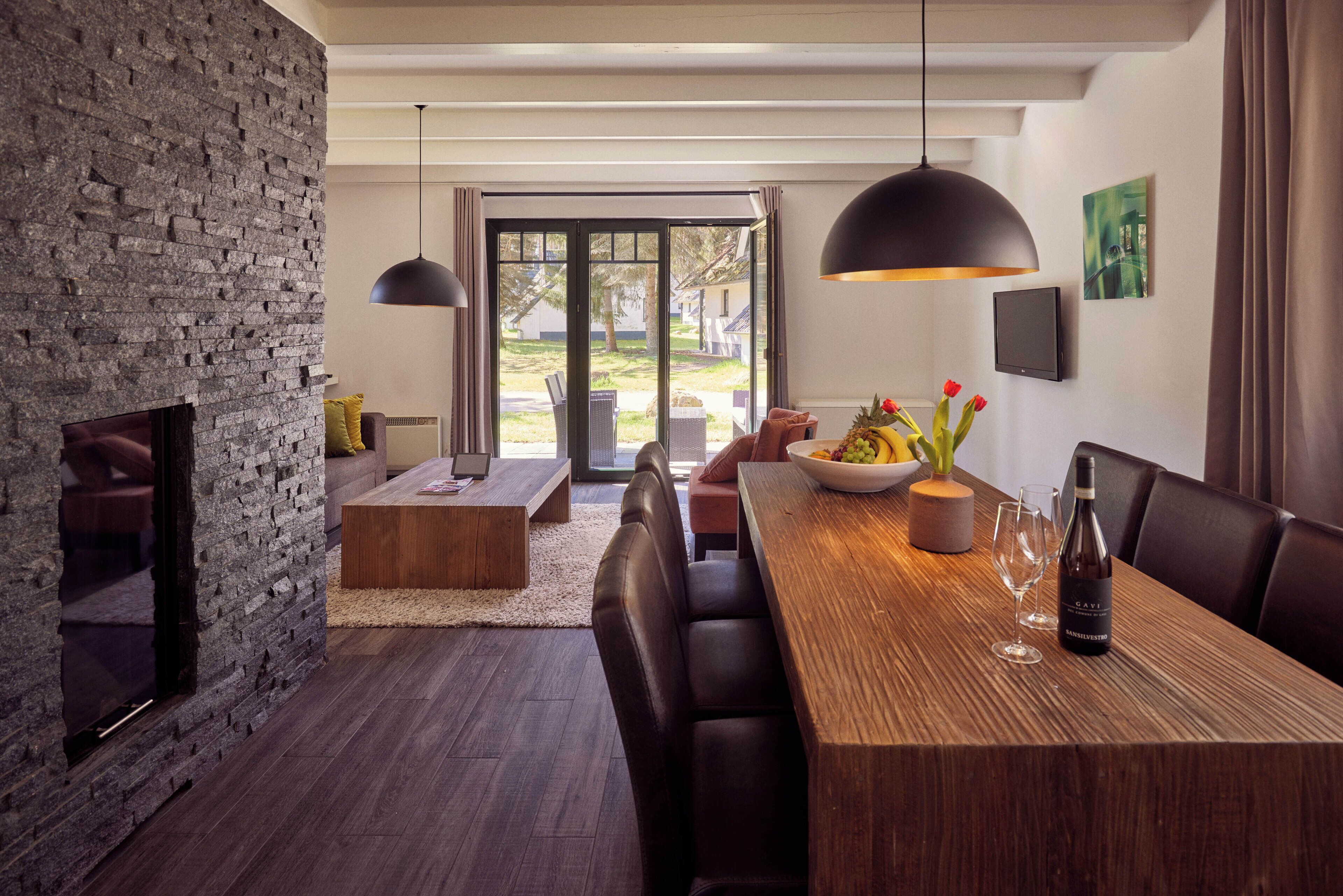 A modern dining area with a wooden table, dark leather chairs, a stone wall, and a view through glass doors.
