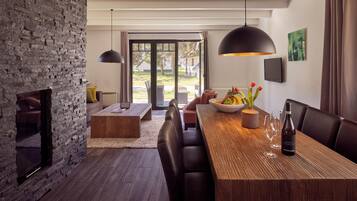 A modern dining area with a wooden table, dark leather chairs, a stone wall, and a view through glass doors.