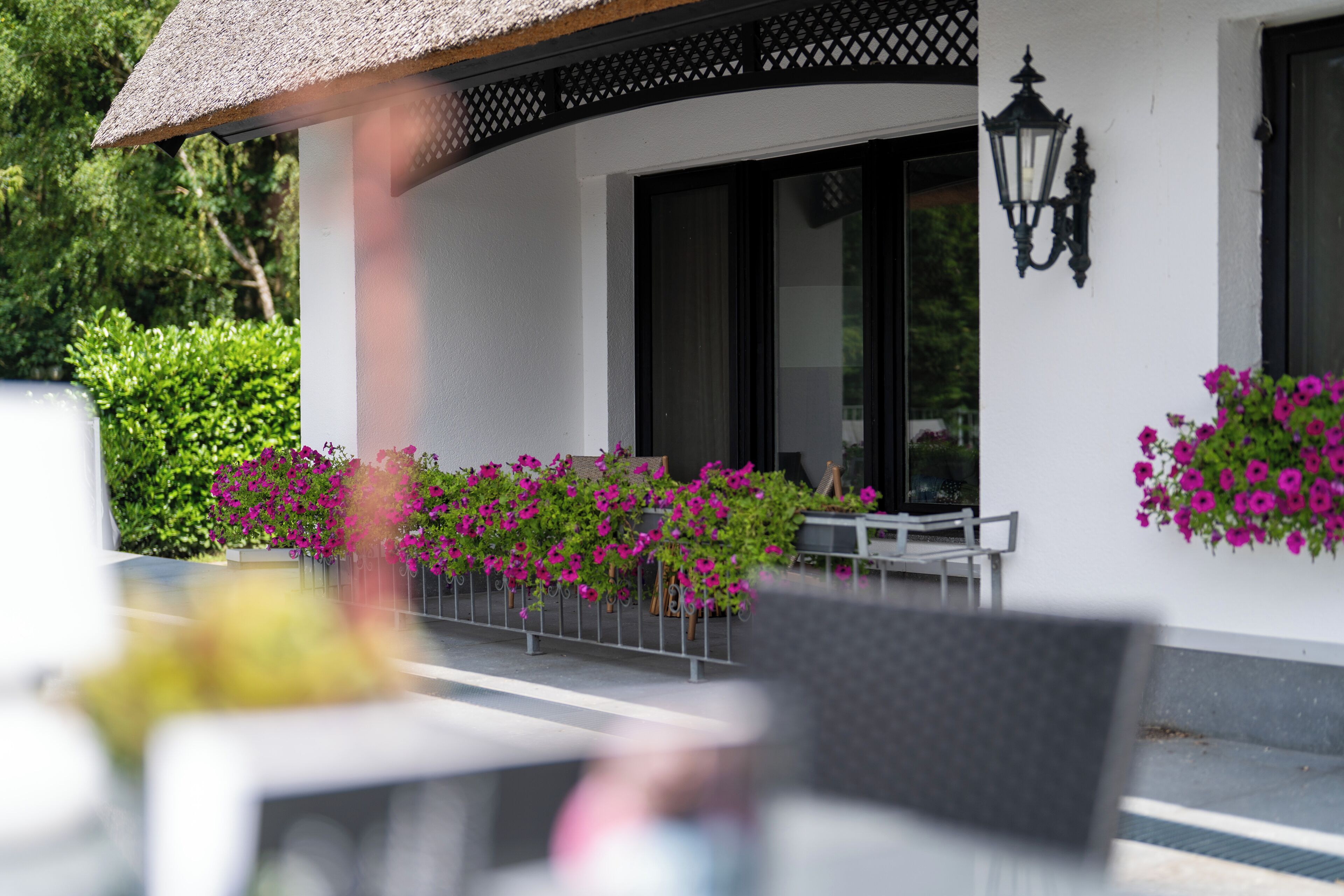 A white building with a thatched roof, a black wall-mounted lamp, and pink flowers in planters.