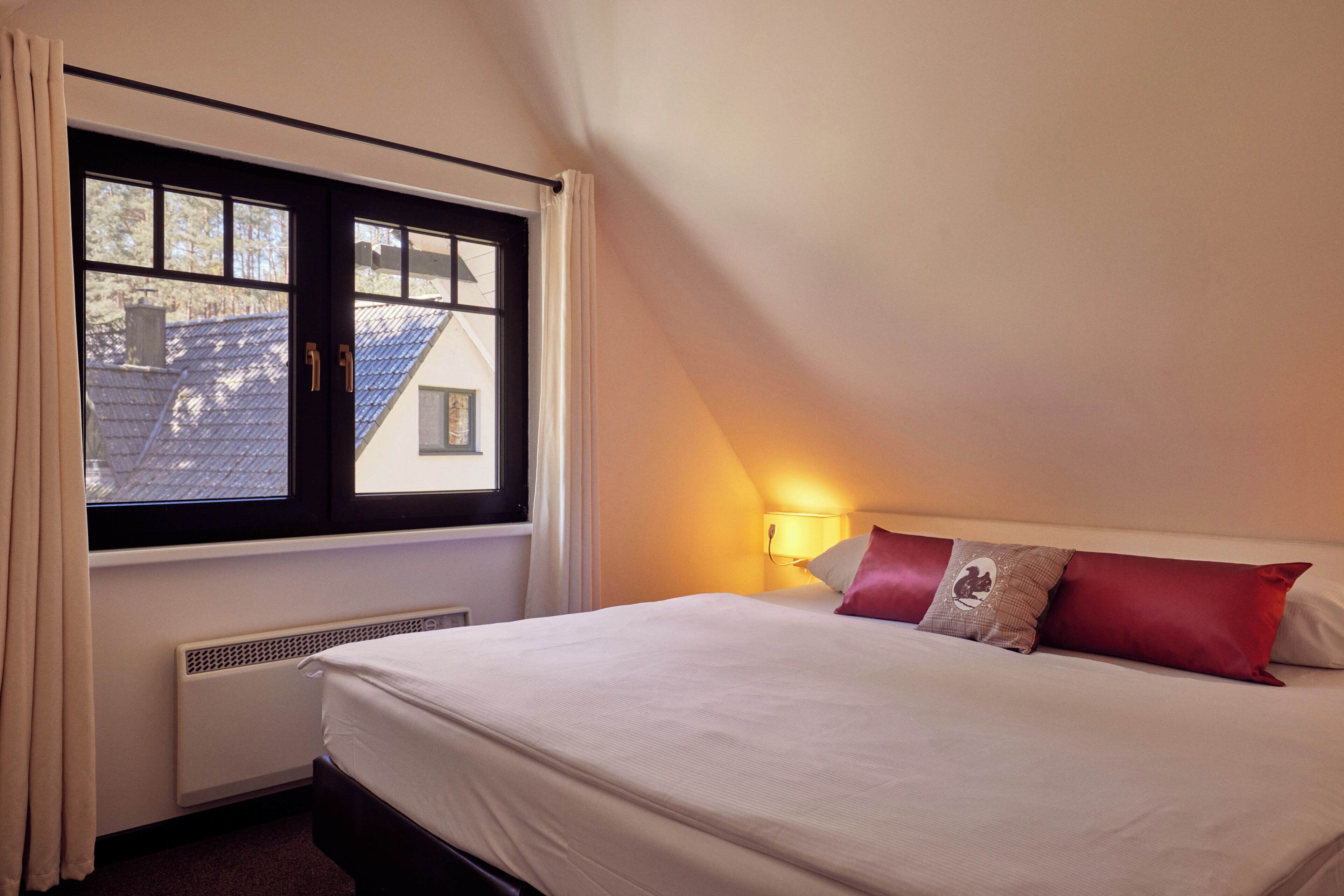 A bedroom with a bed, a window, a radiator, and a wall-mounted lamp.
