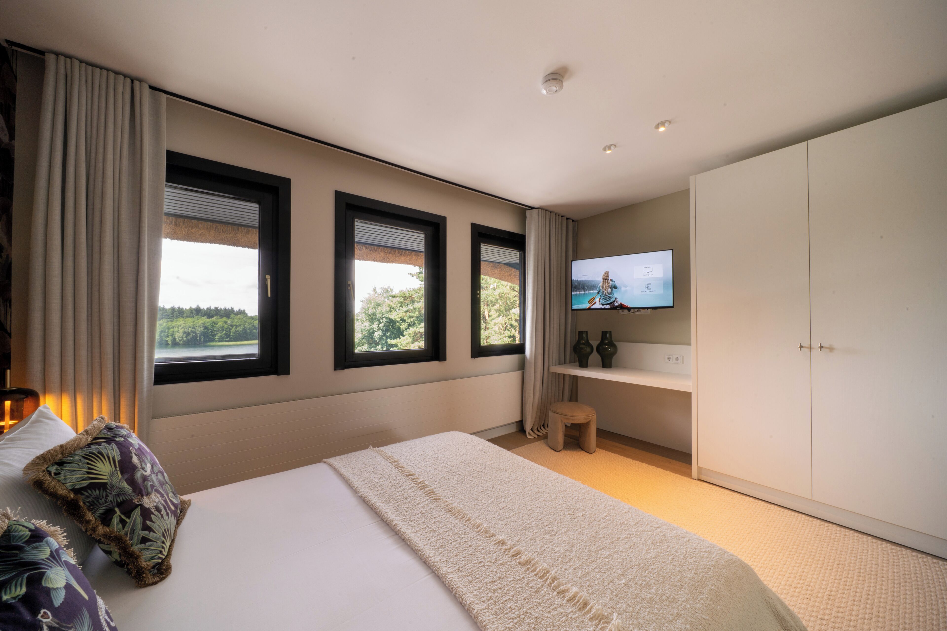 A bedroom with a bed, a television, a wardrobe, and a view of the outdoors.