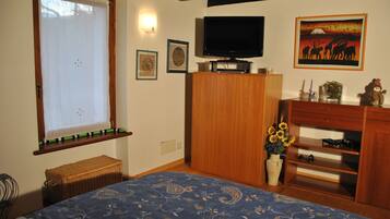 A bedroom with a bed, a television, a wooden wardrobe, a window with a curtain, and a wall with framed pictures.